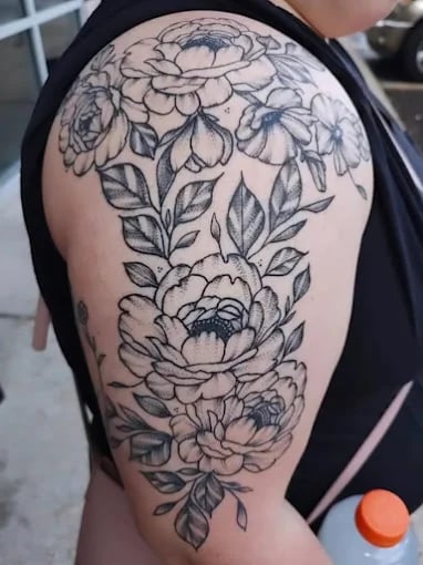 Black and white floral peony tattoo on upper arm with detailed leaves