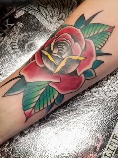 Traditional rose tattoo in vibrant red and green on arm