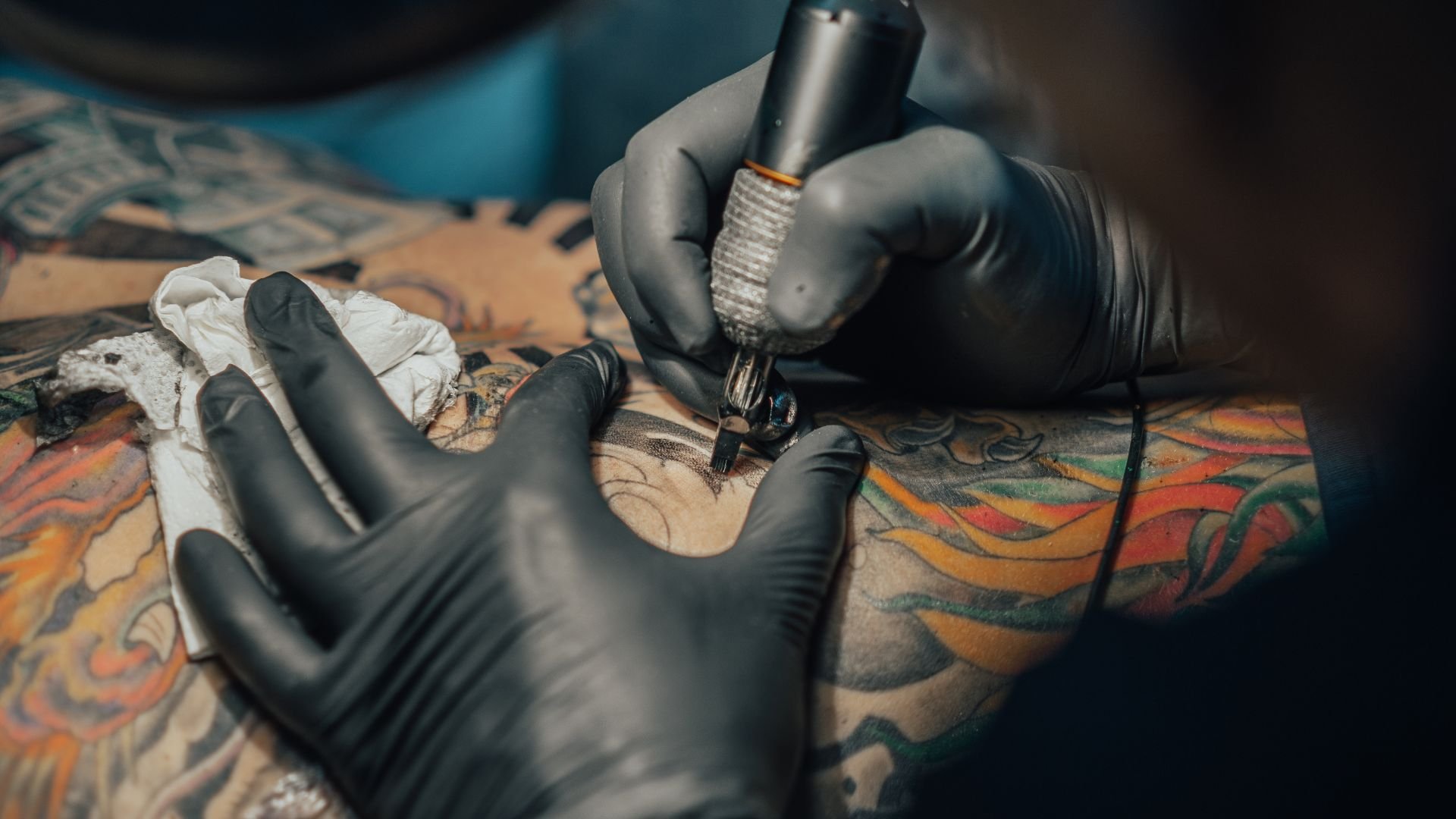 Tattoo artist in black gloves creating colorful artwork on client's arm