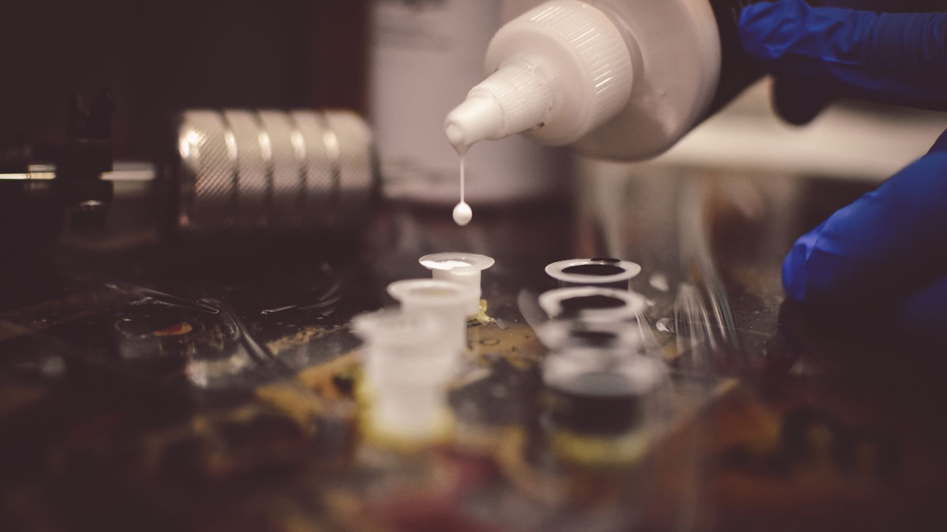 Gloved hand dropping liquid into laboratory test tubes and equipment