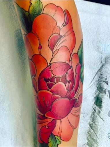 Vibrant colorful peony flower tattoo on skin with red and orange hues