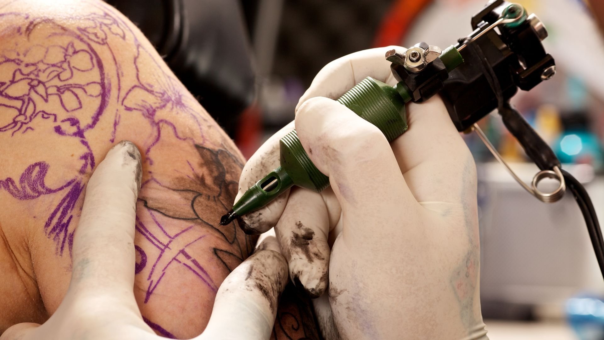 Tattoo artist creating intricate design with purple outline and tattoo machine