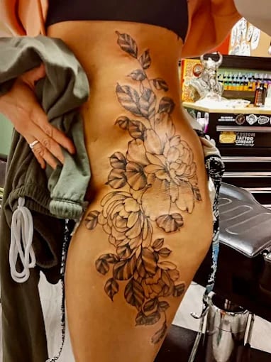 Large floral tattoo of detailed roses and leaves along side of body