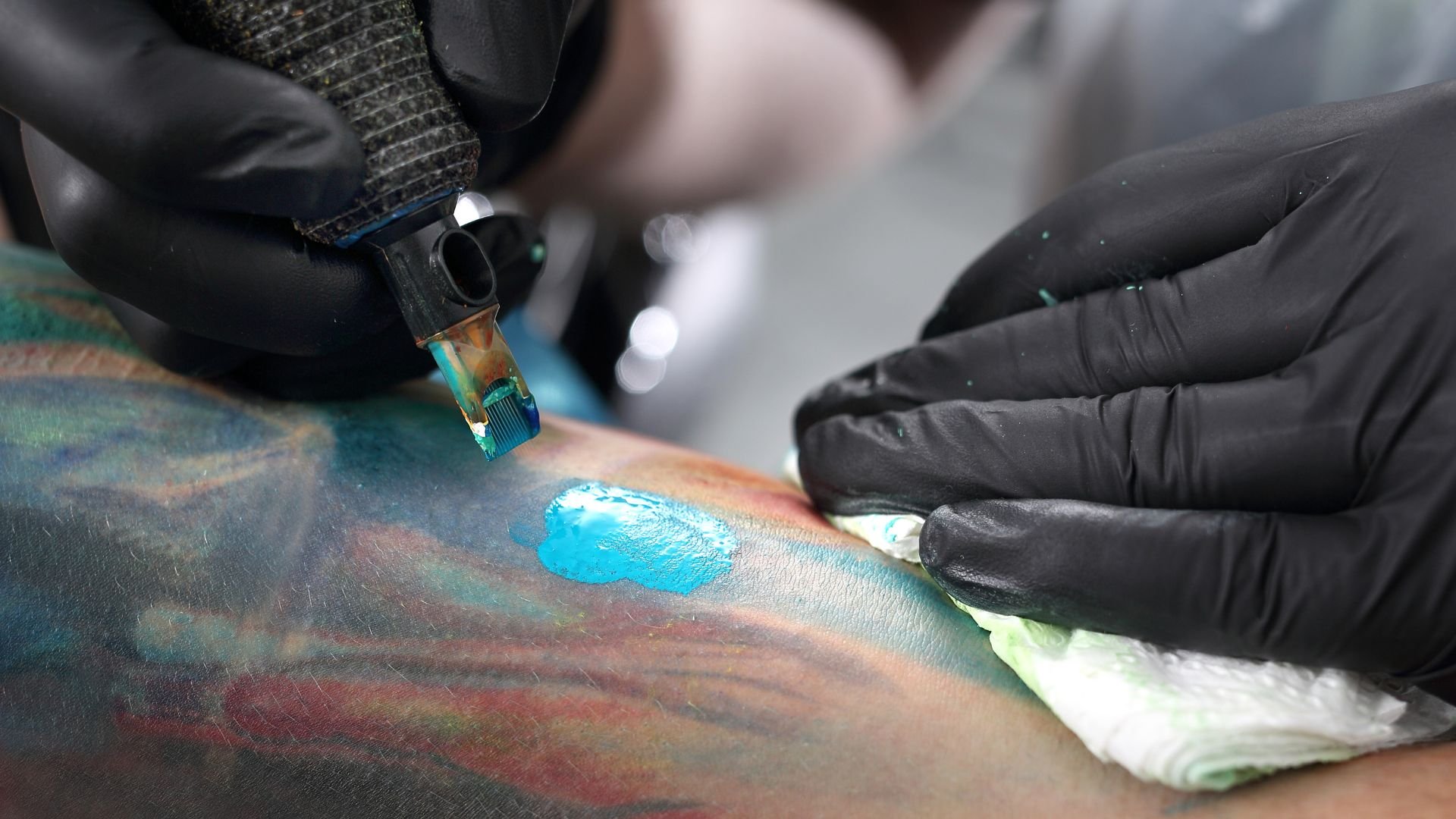 Tattoo artist creates blue ink design on colorful tattooed skin