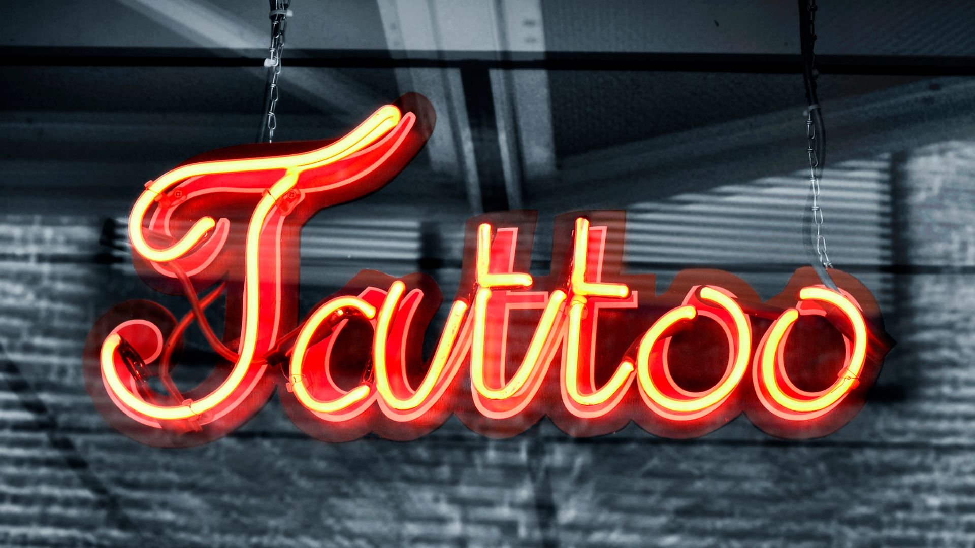 Bright red neon sign spelling "Tattoo" hanging on a dark background