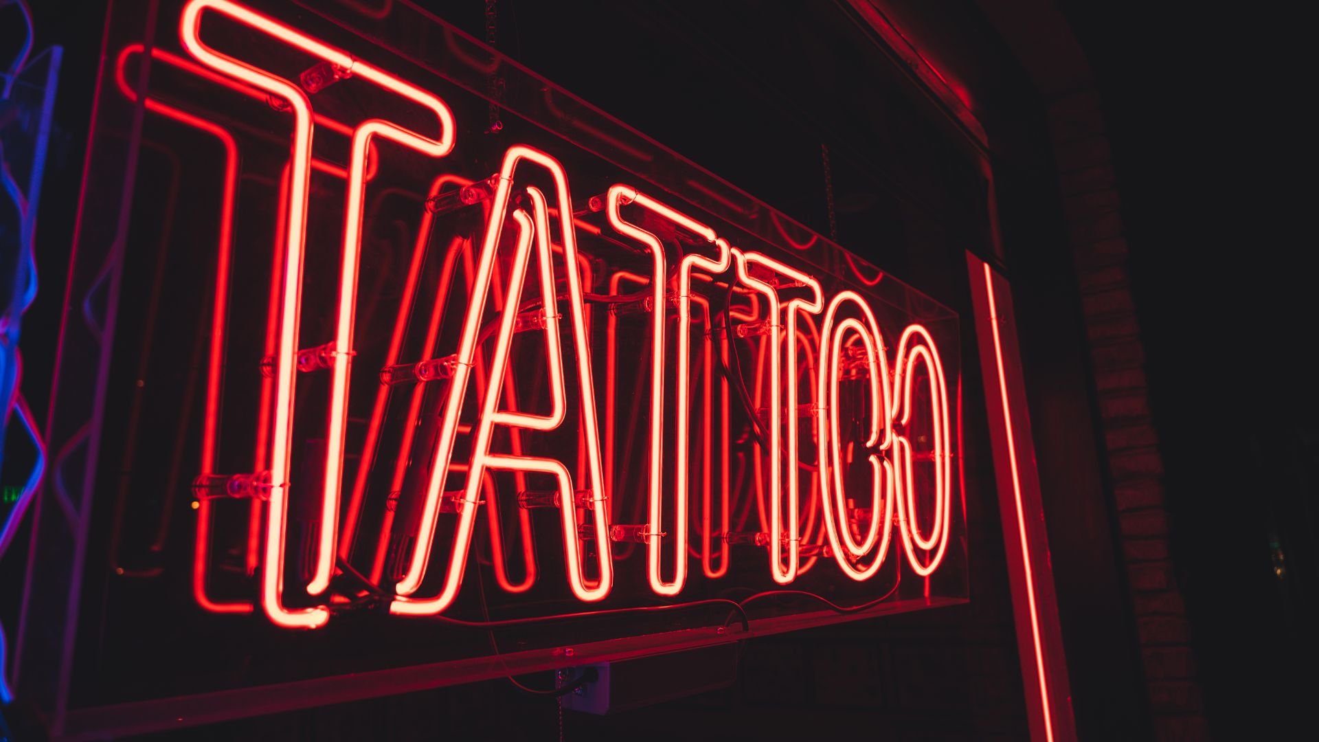 Bright red neon sign spelling out "TATTOO" in dark background